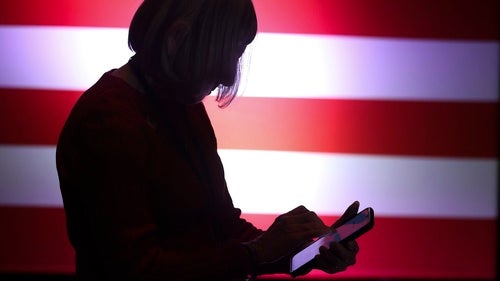 a person looks at their phone in front of an American flag backdrop