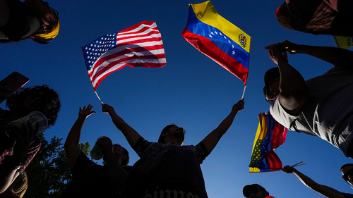 A person waving miniature US and Venezuelan flags in each hand.