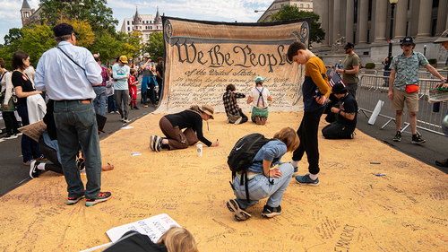 People signing a large banner of the US Constitution at the No Kings protest in Washington