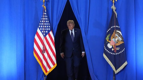 President Donald Trump walks through blue curtains