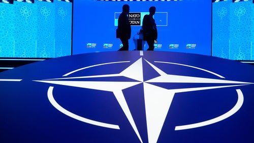 Two men walk past the NATO logo