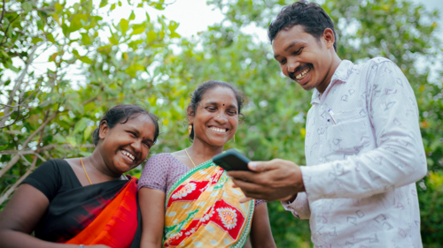 Three people stand together laughing while one holds a mobile phone