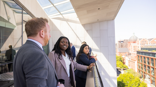 Members of the Emerging Leaders Class of 2026 stand on a balcony and look out onto Washington, DC, during the annual cohort trip in May 2026.