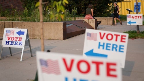 "Vote Here" signs lining a sidewalk outside a voting location.