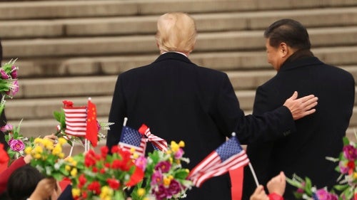President Donald Trump and Chinese President Xi Jinping walk in front of people waving American and Chinese flags