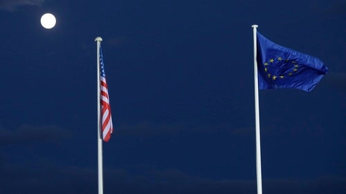 An American flag and an European Union flag fly in a night sky