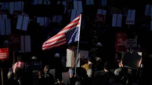 A person in a crowd holds a pole with the American flag hung upside down