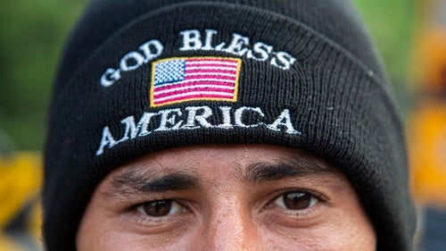 A person wears a hat saying "God Bless America" on the rim