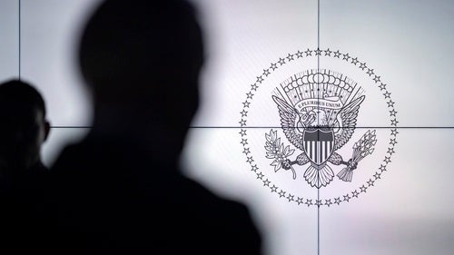 A silhouette of a person in front of the US seal