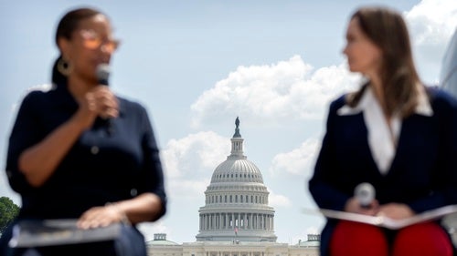 Two people talk in the foreground with the US Capitol building in the background