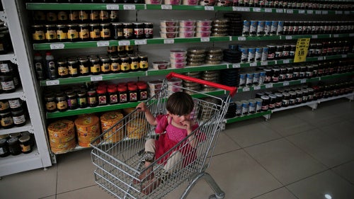 In this Monday, May 16, 2016 photo, two-year old Maria Sheikh, a Syrian refugee child, sits in a trolley at a supermarket in the city of Gaziantep, southeastern Turkey. Maria's mother Huda is using a debit card provided by the World Food Program, to take care partially of the family's groceries. 