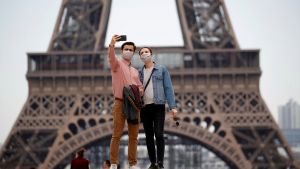 Masked tourists take a photo in front of the Eiffel Tower