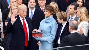 With right hand raised, Donald Trump looks at John Roberts with his back to the camera, as Melania Trump and others watch.