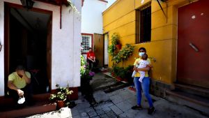 A woman in a mask holds a baby in front of her house in Chile.