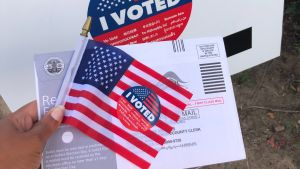 "I voted" sticker with a mail-in ballot and an American flag.