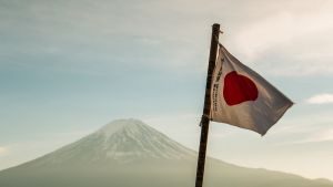 Japan flag waving near a body of water with a mountain in the background