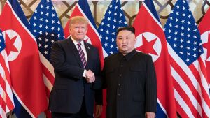 President Trump and Kim Jong Un shake hands in front of US and North Korean flags.