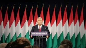 Viktor Orbán speaking at a podium in front of flags.