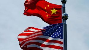 American and China flags, blowing from flagpoles in front of a blue sky