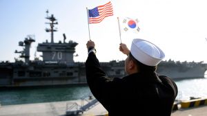 A ROK sailor waves flags in front of an aircraft carrier. 