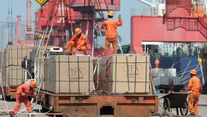 Workers load goods in large boxes for export onto a crane at a port in Lianyungang