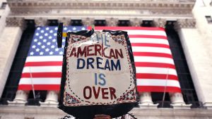 A person holds a sign saying "The American dream is over" outside of Wall Street