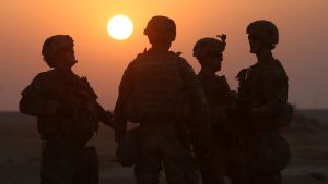 Four US soldiers stand in front of a setting sun