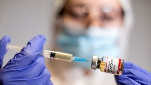 A woman holds a small bottle labeled with a "Coronavirus COVID-19 Vaccine" sticker and a medical syringe in this illustration