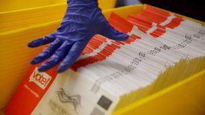 A working wearing gloves sorts through mail-in ballots