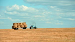 A tractor pulls a trailer with stacked bails of hay.