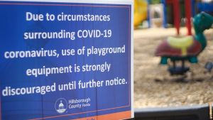 Park closure sign with empty playground in background.