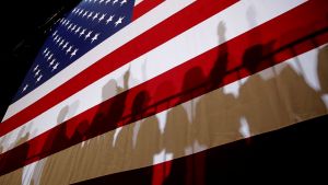 Shadows cast from a crowd of people in front of an American flag.