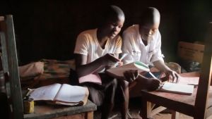 Two young people do schoolwork with books and notebooks in hand