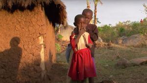 Two children stand together outside of a house