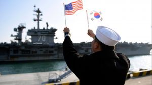 A ROK sailor waves flags in front of an aircraft carrier. 