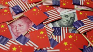 A US dollar banknote featuring American founding father Benjamin Franklin and a China's yuan banknote featuring late Chinese chairman Mao Zedong are seen among US and Chinese flags.