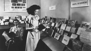 A black and white photo of a person browsing the Council pamphlet shop in the 1940s.