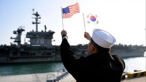 A ROK sailor waves flags in front of an aircraft carrier. 