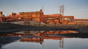 An exterior shot of a factory in the rust belt at sunset, with a puddle of water in the foreground