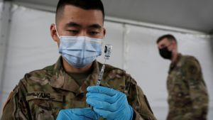 A US Army soldier wearing gloves and a surgical mask prepares a COVID-19 vaccine