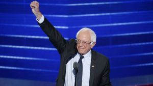 Bernie Sanders stands behind a podium with his fist in the air