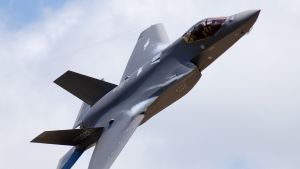 A close-up image of a military plane in the air with clouds.