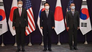 Sung Kim, Noh Kyu-duk, and Takehiro Funakoshi standing in front of flags on flag poles