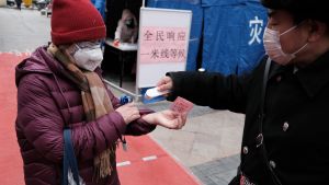A person wearing a surgical mask gets temperature checked on their wrist.