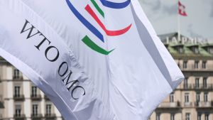 A flag with the letters WTO OMC waves in front of the World Trade Organization headquarters.