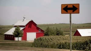 A photo of a red barn with a t-intersection street sign in the foreground