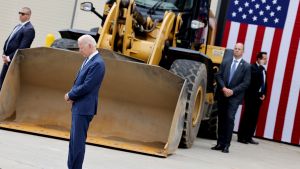 President Biden stands in front of a bulldozer and American flag.