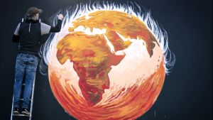 An artist finishes a mural of the earth on fire with the caption "while you were talking."