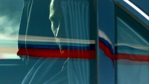 President Putin looks out a car window with the Russian flag reflected on it.
