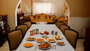 A table set with various foods on a white tablecloth before an archway and a window.